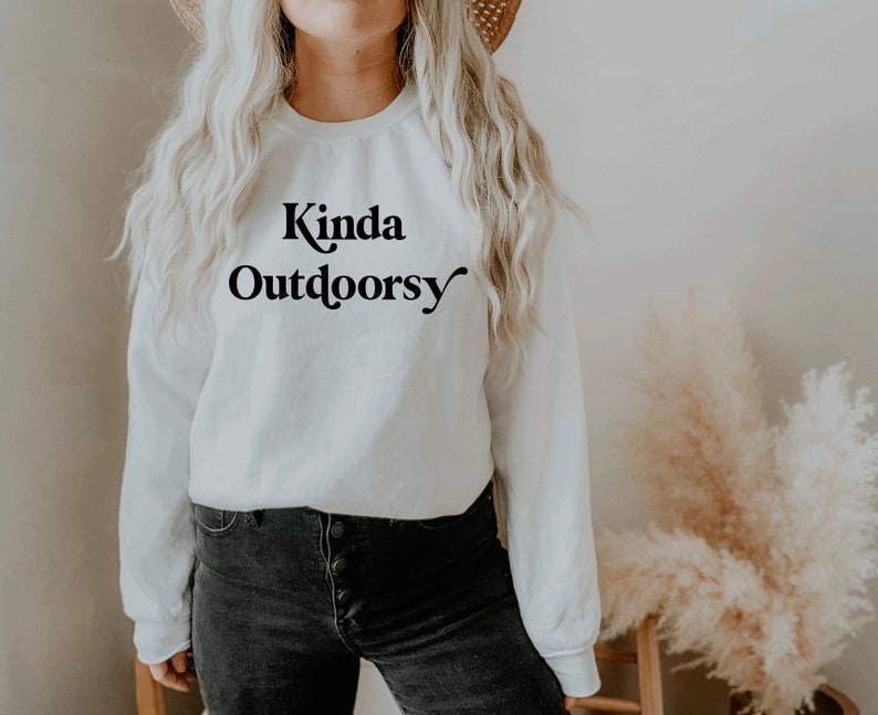 May include: White long-sleeve sweatshirt with the text "Kinda Outdoorsy" in black lettering.