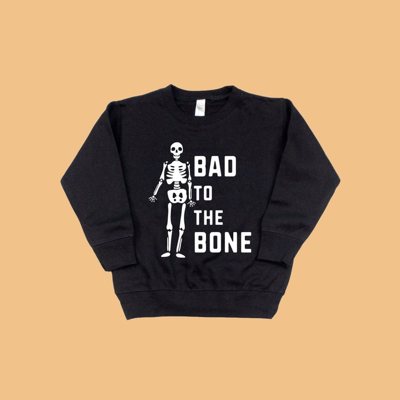 Pu&ograve; includere: Felpa nera con un grafico di scheletro bianco e il testo "Bad to the Bone".