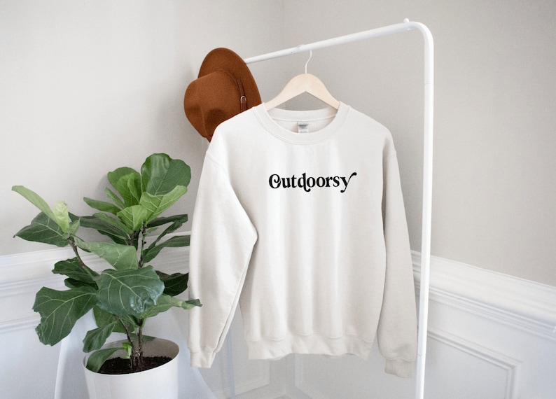 May include: A cream colored sweatshirt with the word "Outdoorsy" printed in black on the front.