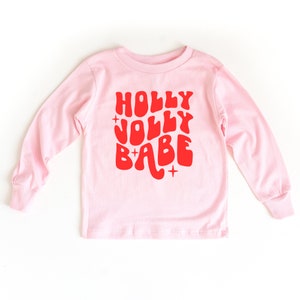 May include: Pink long-sleeved shirt with a red graphic that says "HOLLY JOLLY BABE" in a retro font.