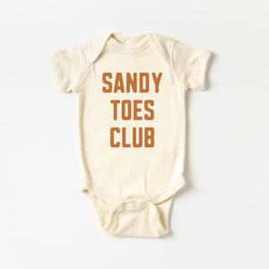 May include: A cream-colored baby onesie with the text "SANDY TOES CLUB" printed in orange.