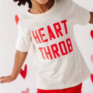May include: A white t-shirt with the words "HEART THROB" printed in red.