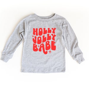 May include: A gray long-sleeved shirt with a red graphic that says "HOLLY JOLLY BABE" in a retro font.