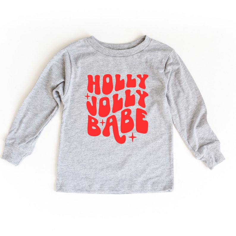 May include: A gray long-sleeved shirt with a red graphic that says "HOLLY JOLLY BABE" in a retro font.