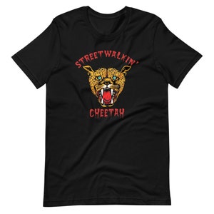 以下が含まれることがあります： 赤い「Streetwalkin' Cheetah」の文字と、赤いチーターの顔のグラフィックがプリントされた黒いTシャツ