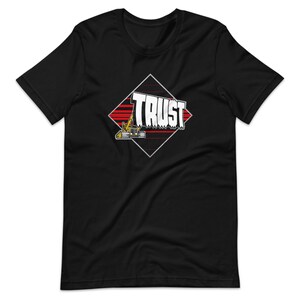 May include: Black t-shirt featuring a graphic design with the word "TRUST" in white, set within a diamond shape with red stripes and a yellow and black excavator. A crew neck, short-sleeve tee.