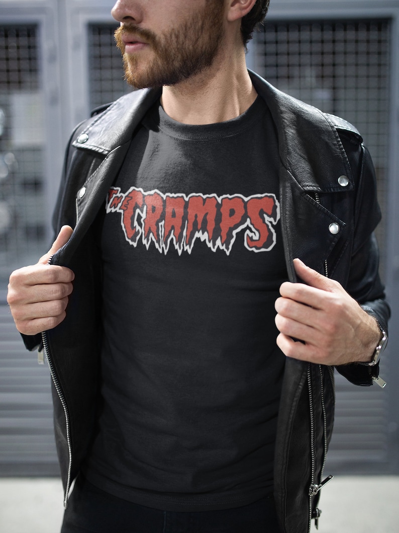 May include: A black t-shirt with a red "The Cramps" logo printed on the front. The logo is in a dripping font style.