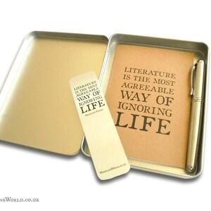 May include: A silver metal tin with a brown paper insert and a silver pen. The paper insert has the text "Literature is the most agreeable way of ignoring life" printed on it. The tin also includes a bookmark with the same text printed on it.
