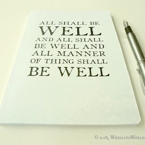 May include: White notebook with the text "ALL SHALL BE WELL AND ALL SHALL BE WELL AND ALL MANNER OF THING SHALL BE WELL" printed in black. The notebook is lying on a white surface with a silver pen next to it.