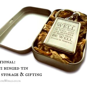 May include: A silver keychain with the quote "All shall be well and all shall be well and all manner of thing shall be well" by Julian of Norwich. The keychain is in a small, silver tin with brown tissue paper.