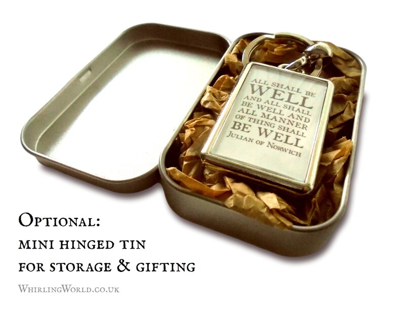 May include: A silver keychain with the quote "All shall be well and all shall be well and all manner of thing shall be well" by Julian of Norwich. The keychain is in a small, silver tin with brown tissue paper.