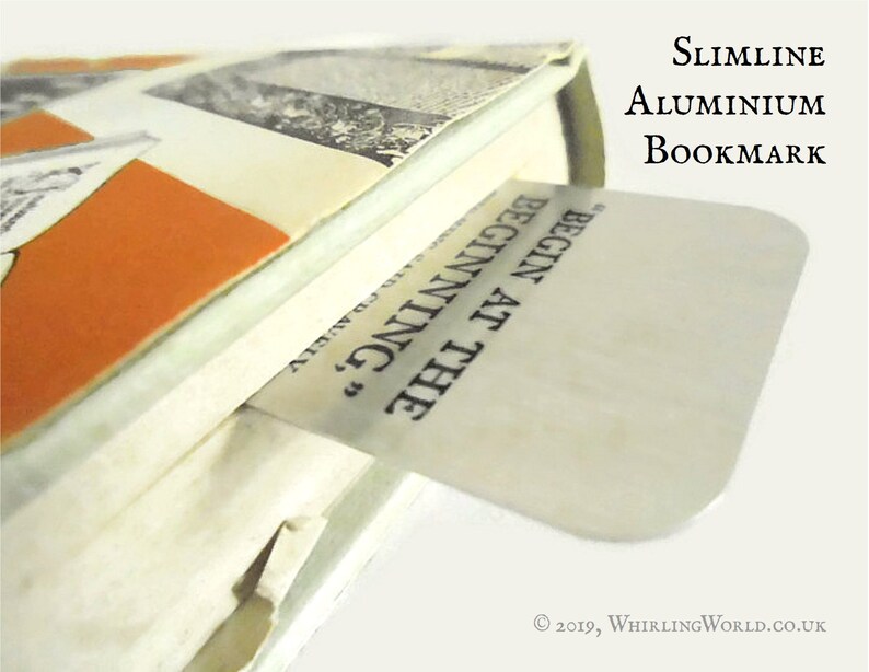 May include: A silver bookmark with the text "BEGIN AT THE BEGINNING" printed on it. The bookmark is made of slimline aluminum.