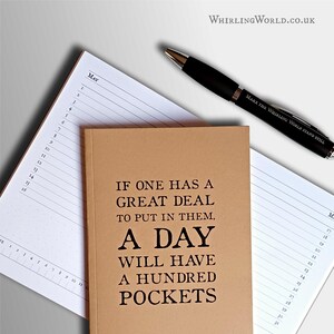 May include: A tan notebook with the black text "IF ONE HAS A GREAT DEAL TO PUT IN THEM, A DAY WILL HAVE A HUNDRED POCKETS" resting on an open white planner page with May dates listed, accompanied by a black pen inscribed "MAKE THE WHIRLING WORLD STAND STILL."
