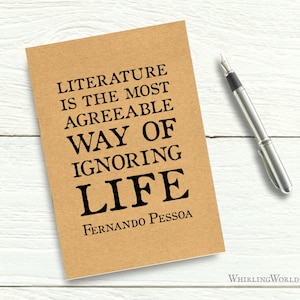 May include: A brown notebook with the quote "Literature is the most agreeable way of ignoring life" by Fernando Pessoa printed on the front.