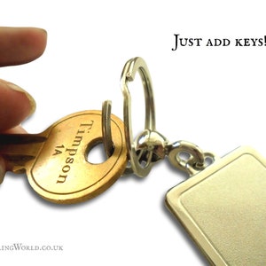 May include: A silver key chain with a blank rectangular tag and a silver split ring. A brass key with the inscription "Trimpson 1A" is attached to the ring. The text "JUST ADD KEYS!" is visible in the upper right corner of the image.