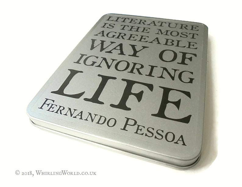 May include: A silver metal box with the quote "Literature is the most agreeable way of ignoring life" by Fernando Pessoa printed on the front.