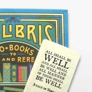 May include: A gold bookmark with a white background and black text. The text reads "All shall be well and all shall be well and all manner of thing shall be well. Julian of Norwich."