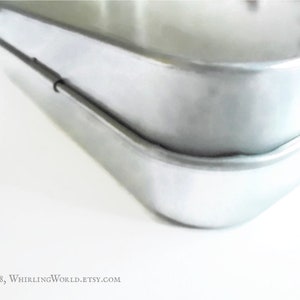May include: Close-up of the edge of a silver baking pan. The pan has a smooth, shiny surface and a slightly rounded edge.