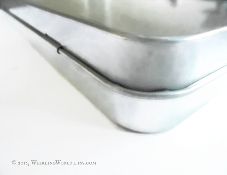 May include: Close-up of the edge of a silver baking pan. The pan has a smooth, shiny surface and a slightly rounded edge.