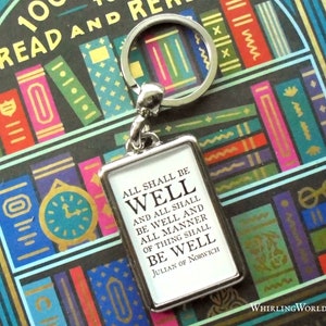 May include: A silver keychain with a small rectangular tag that reads "All shall be well and all shall be well and all manner of thing shall be well Julian of Norwich". The keychain is in front of a book with a colorful bookshelf design.
