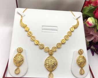 May include: A gold necklace and earrings set with a delicate, intricate design. The necklace features a pendant with a circular shape and a drop-shaped design. The earrings are also circular with a drop-shaped design.