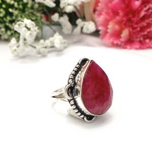 以下が含まれることがあります： 装飾的な銀のセッティングにセットされた、大きな涙型の濃い赤色の宝石が付いた銀のリングです。