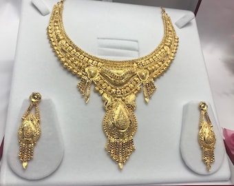 May include: A gold necklace and earrings set with intricate designs. The necklace features a large pendant with a teardrop shape and a delicate chain. The earrings are small and dangle.