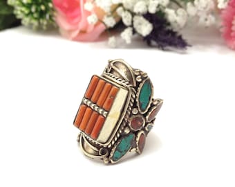 May include: A silver ring with a square-shaped coral stone set in the center. The ring is decorated with turquoise and red stones.