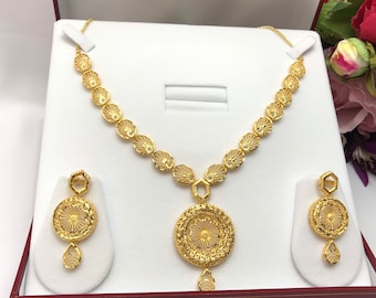 May include: A gold necklace and earrings set with a delicate floral design. The necklace features a pendant with a round, openwork design and a small drop. The earrings are also round and feature a similar openwork design.