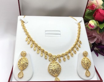 May include: A gold necklace and earrings set with a delicate, intricate design. The necklace features a pendant with a circular, openwork design and a drop-shaped detail. The earrings are similarly designed with a circular pendant and a drop.