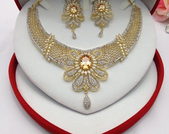 May include: A gold necklace and earrings set with a large, clear, yellow gemstone surrounded by smaller, clear stones. The set is displayed in a red velvet box.