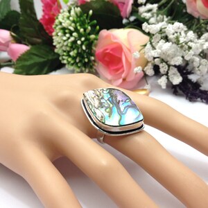 Può includere: Un anello d'argento con un grande guscio di abalone iridescente incastonato in una ghiera d'argento. L'anello è su una mano di manichino.