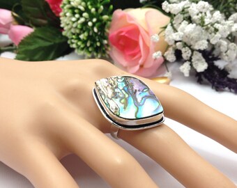 May include: A silver ring with a large iridescent abalone shell set in a silver bezel. The ring is on a mannequin hand.