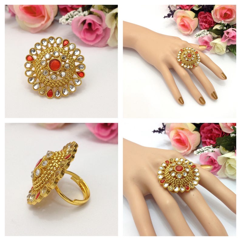 May include: A gold ring with a large, round, red and white gemstone design. The ring is set against a white background.