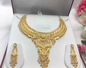 May include: A gold necklace and earrings set with intricate designs. The necklace features a large pendant with a cascading design. The earrings are long and dangle.