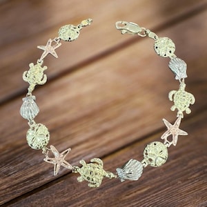 Può includere: Un braccialetto d'oro con una varietà di ciondoli a tema marino, tra cui conchiglie, stelle marine e tartarughe marine. Il braccialetto è realizzato in tre diverse tonalità d'oro, creando un design unico e accattivante.