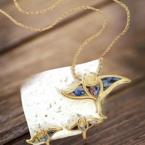 Op de afbeelding: Een gouden ketting- en oorstekerset met een manta-roggenhanger en oorbellen van iriserende parelmoer. De ketting heeft een touwkettingstijl.