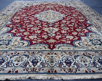 Puede incluir: Una alfombra rectangular grande con un campo central rojo adornado con motivos florales. El borde es de color crema con detalles en azul y beige. La alfombra tiene un borde con flecos y detalles intrincados.