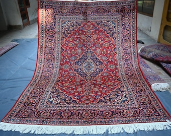 Puede incluir: Una alfombra persa tradicional con un esquema de color rojo, azul y marfil. La alfombra tiene un medallón central con intrincados diseños florales y un borde con patrones repetidos.