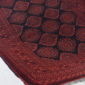 May include: A red and black patterned rug with a geometric design. The rug has a fringed border.