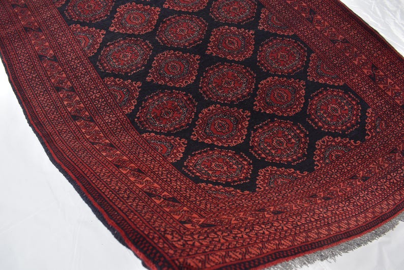 May include: A red and black patterned rug with a geometric design. The rug has a fringed border.