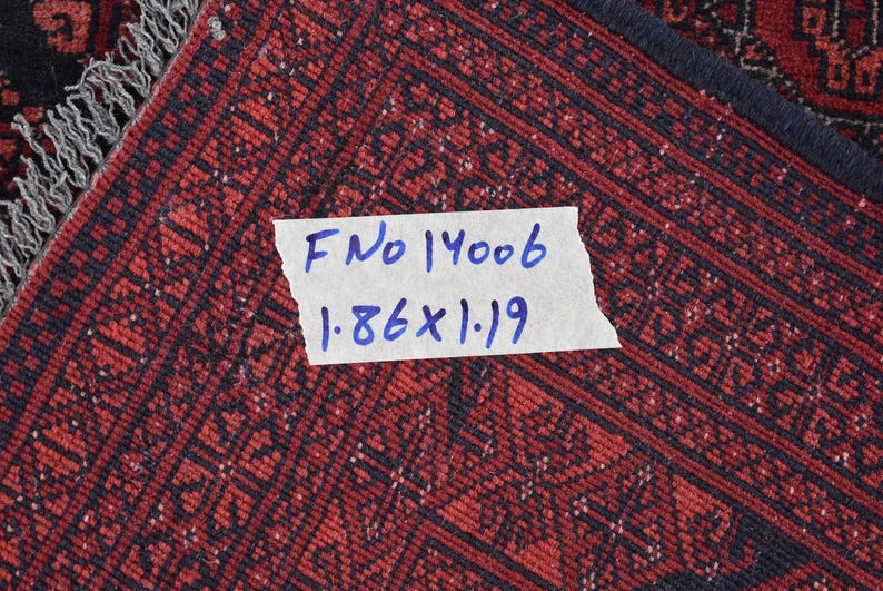 May include: Close-up of a red and black patterned rug with a white label that reads "F No 14006 1.86 x 1.19".
