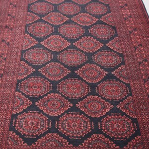 May include: A traditional Persian rug with a dark blue background and intricate red and white floral patterns. The rug has a border with a repeating geometric design.