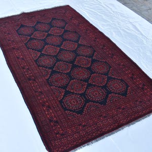 May include: A red and blue patterned rug with a geometric design. The rug has a fringed border.