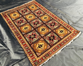 Op de afbeelding: Een traditioneel tapijt met een geometrisch patroon in tinten rood, bruin, geel en blauw. Het tapijt heeft een gefranst randje.