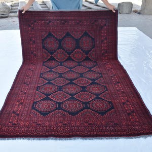 May include: A red and black patterned rug with a geometric design. The rug has a fringed border and is folded in half.