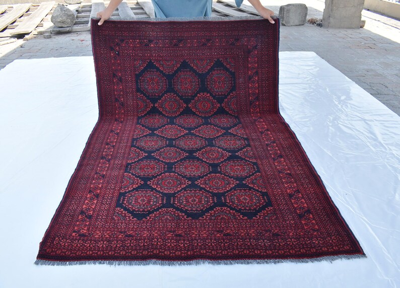 May include: A red and black patterned rug with a geometric design. The rug has a fringed border and is folded in half.