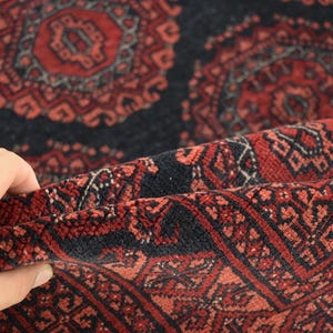 May include: Close-up of a red and black patterned rug with intricate designs. The rug is folded in half, revealing the underside of the fabric.