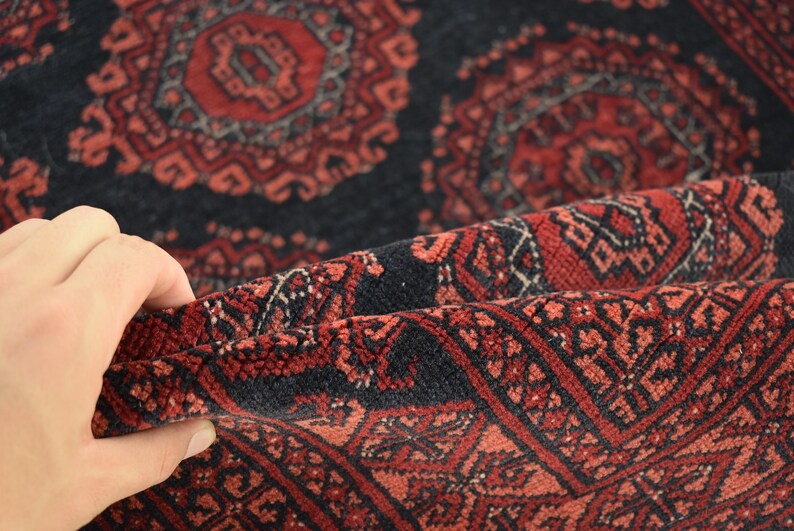 May include: Close-up of a red and black patterned rug with intricate designs. The rug is folded in half, revealing the underside of the fabric.