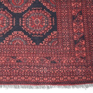 May include: A red and black patterned rug with a geometric design. The rug has a fringed border.